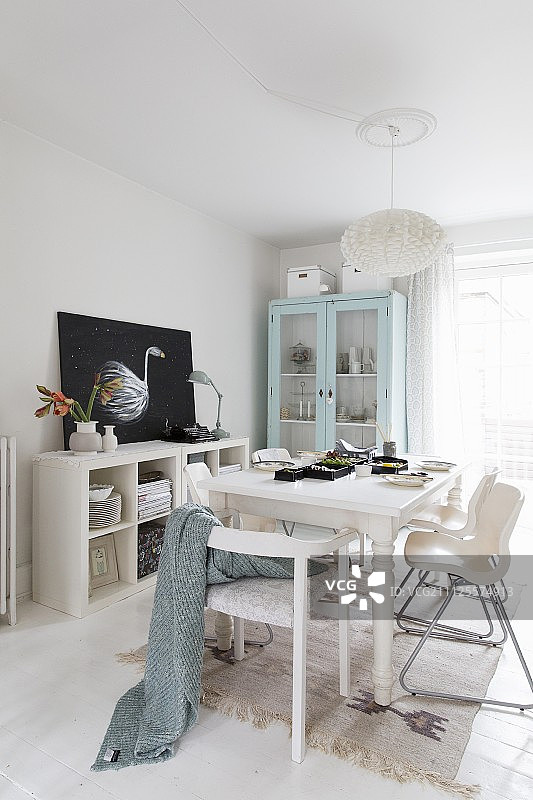 木桌周围摆放着现代椅子的白色用餐区，背景是粉彩展示柜图片素材