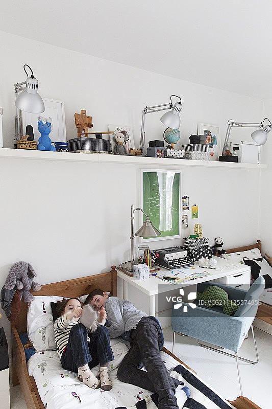 兄妹卧室：木床间的白色书桌、悬挂的置物架和躺在床上的男孩女孩图片素材