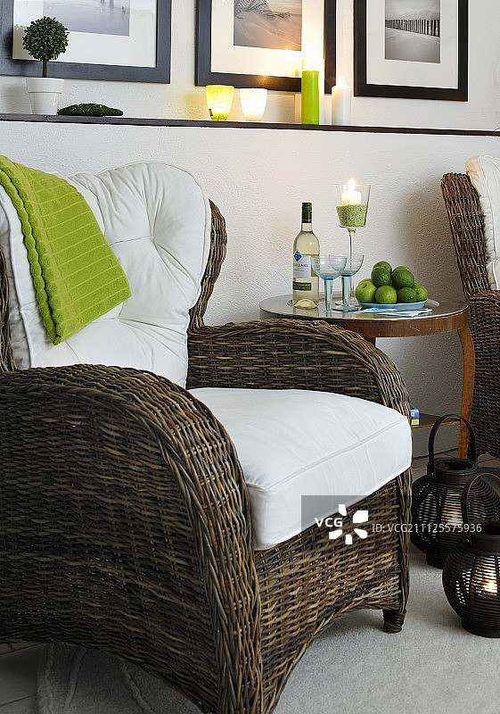 白色靠垫柳条扶手椅，烛光氛围中的葡萄酒瓶和酒杯边桌图片素材