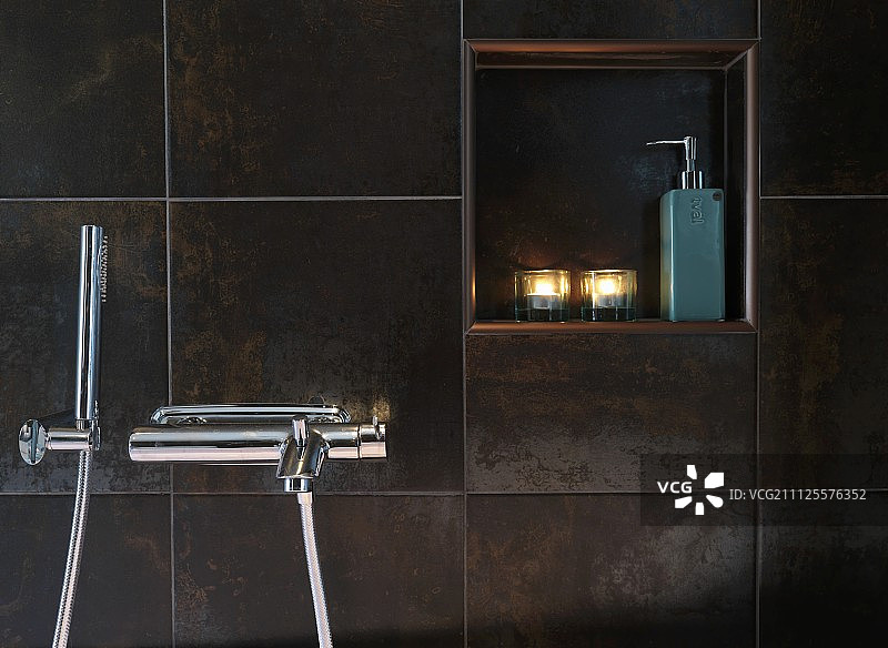 墙壁壁龛中的蜡烛和分配瓶，配有深锈色瓷砖和现代壁挂式水龙头图片素材