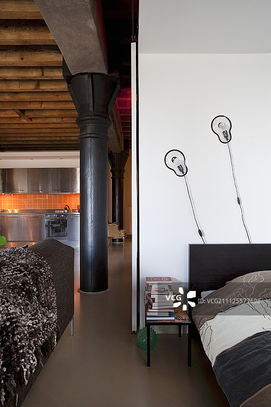 阁楼公寓的开放式睡眠区，配有设计师壁灯，可欣赏黑色金属柱和不锈钢厨房的景色图片素材