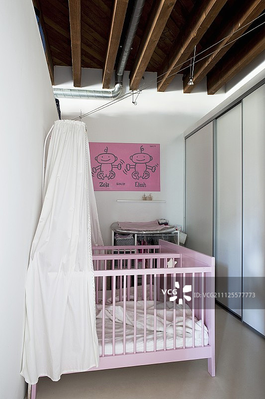粉色双人婴儿床，配有白色天篷和嵌入式衣柜，位于质朴的木梁天花板下图片素材