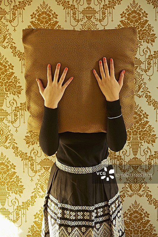 涂有指甲油的女人拿着靠垫站在带有金色华丽图案的墙纸前图片素材