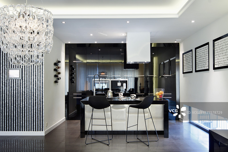 现代室内开放式厨房的吧台黑色吧台椅，带有间接天花板照明和一侧的枝形吊灯图片素材