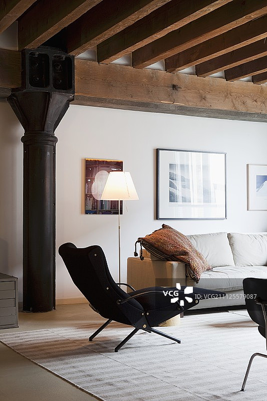 复古风格黑色扶手椅，带脚凳和落地灯，位于具有工业风格的阁楼公寓沙发旁图片素材