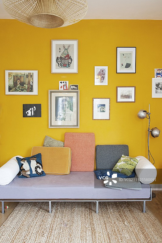 黄色墙壁上图片下方的简易沙发上放着各种靠垫图片素材
