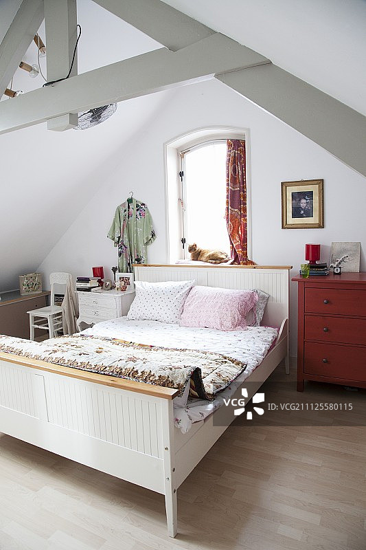 简朴阁楼房间内的白色木制框架乡村雪橇床，带有外露的木制屋顶结构图片素材