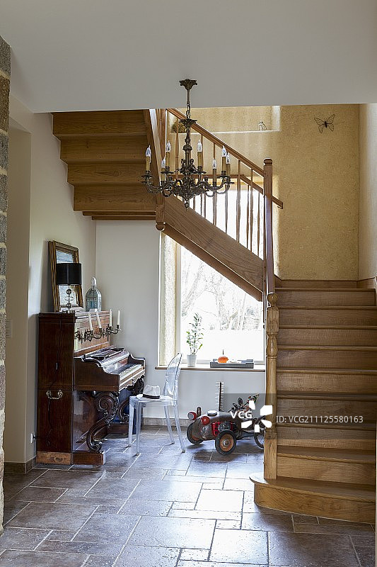 瓷砖走廊中的木制楼梯，配有古董钢琴和复古玩具车图片素材