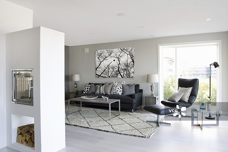 休息区内的砖石壁炉，配有灰色油漆墙壁、黑色皮革休闲椅和脚凳图片素材