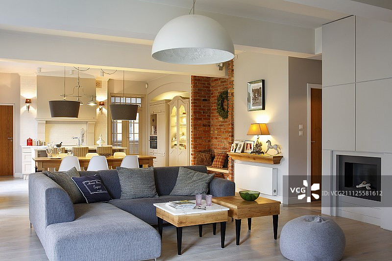 现代灰色转角沙发和小木制边桌，位于开放式乡村风格室内用餐区前图片素材