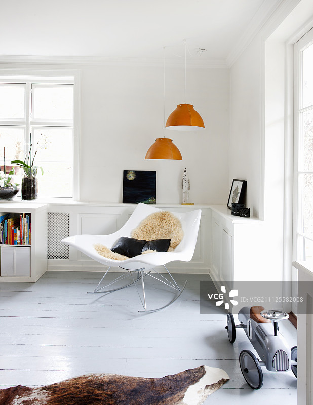 客厅角落里橙色吊灯下的设计师摇椅，旁边灰色地板上放着复古玩具车图片素材