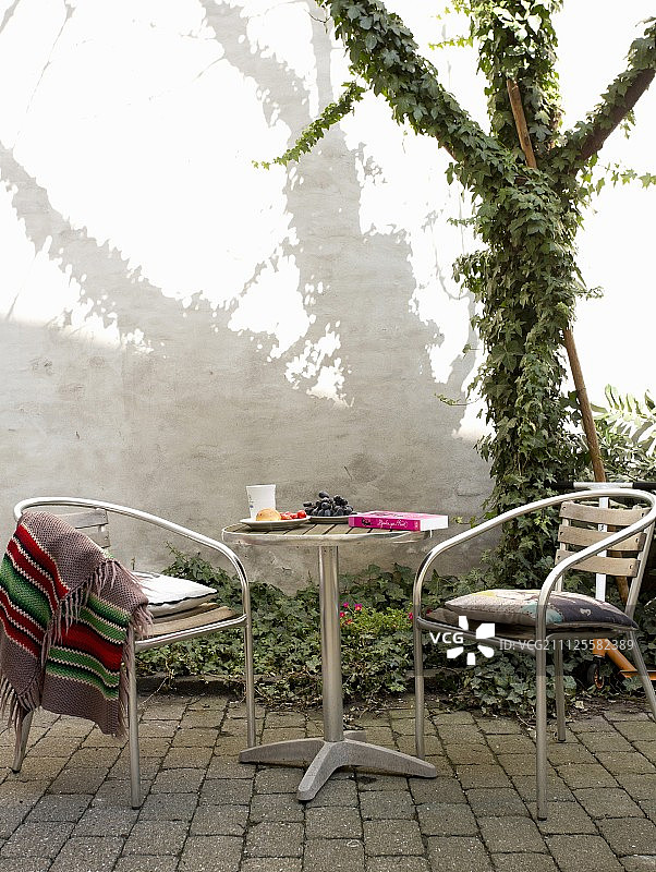 露台休息区，配有小酒馆家具、铺砌地板和庭院中覆盖常春藤的树木图片素材