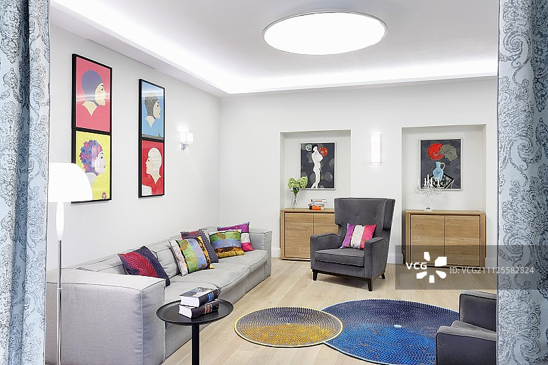 灰色沙发和扶手椅上的彩色靠垫，墙壁上的彩色艺术品和地板上的圆形地毯图片素材