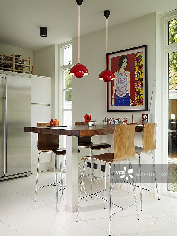 带有不锈钢底座、木质外壳吧台凳、红色吊灯和法式窗户的柜台图片素材