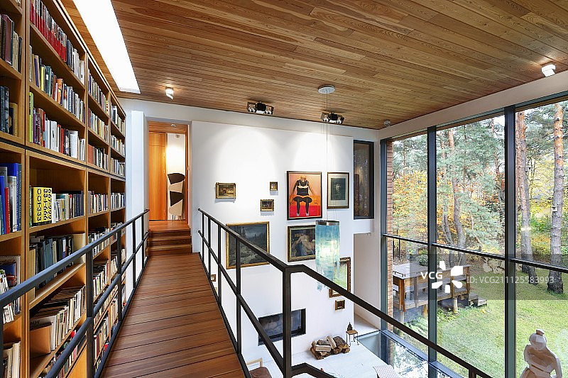 通风的钢木画廊上的书柜，与玻璃墙相对，尽头墙上有一排画图片素材