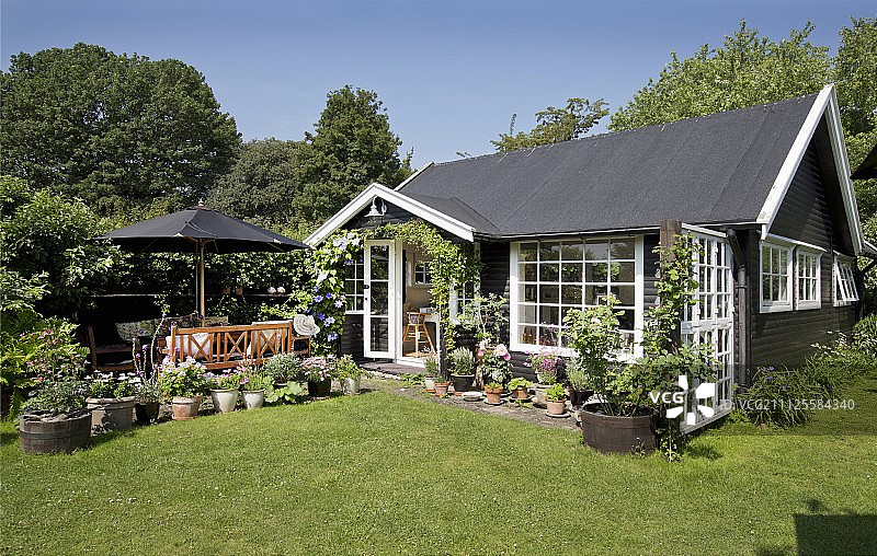阳光明媚的花园中带有白色格子窗的黑色夏季小屋图片素材