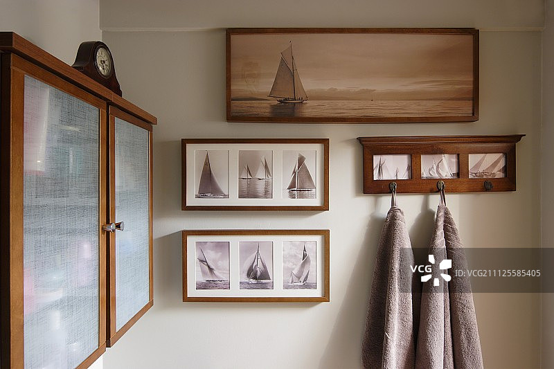 帆船相框照片和挂在墙钩上的毛巾；一侧是带不透明玻璃门的木制壁柜图片素材