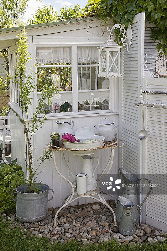 花园棚屋外墙上生锈金属支架上的复古洗脸盆和水罐图片素材