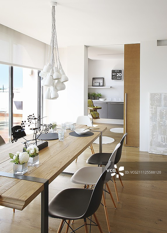 简约设计师木桌和伊姆斯塑料椅上方的灯具；通往厨房的推拉门在背景中图片素材