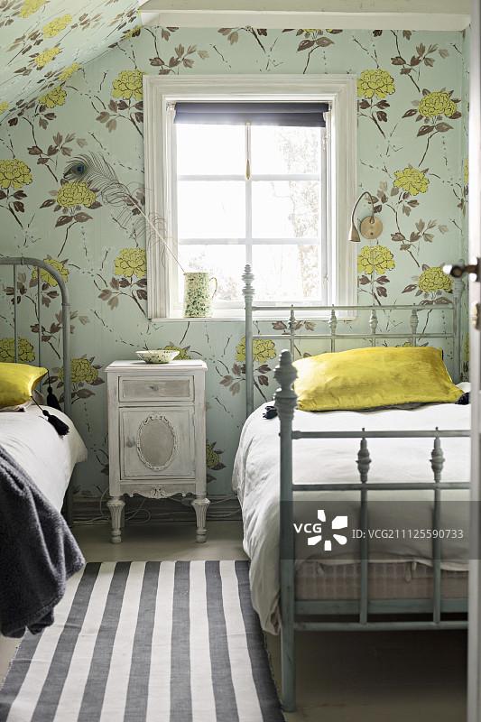 复古风格卧室，带有花卉壁纸和床头柜，双人金属床，窗户下方框架漆成灰色图片素材