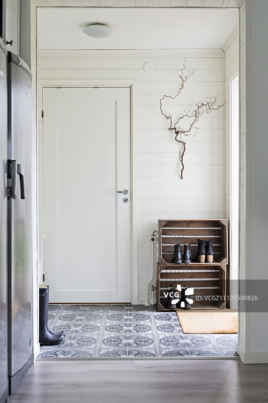 透过落地开放式门望向门厅，鞋架靠在白色木墙和复古图案地砖上图片素材