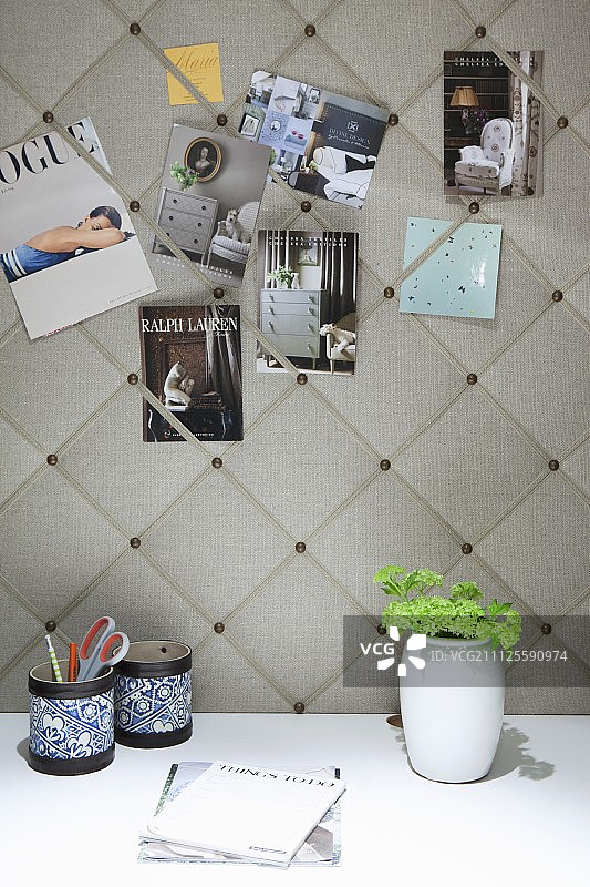 贴在雅致的织物软木板上的明信片，白色桌子上有笔筒和花瓶图片素材