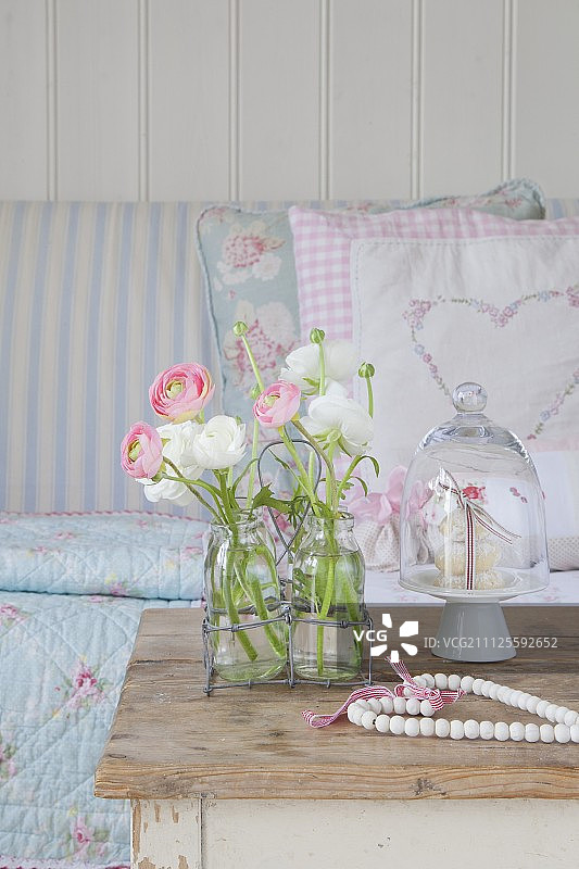 玻璃瓶毛茛花，置于旧沙发前的蛋糕架上图片素材