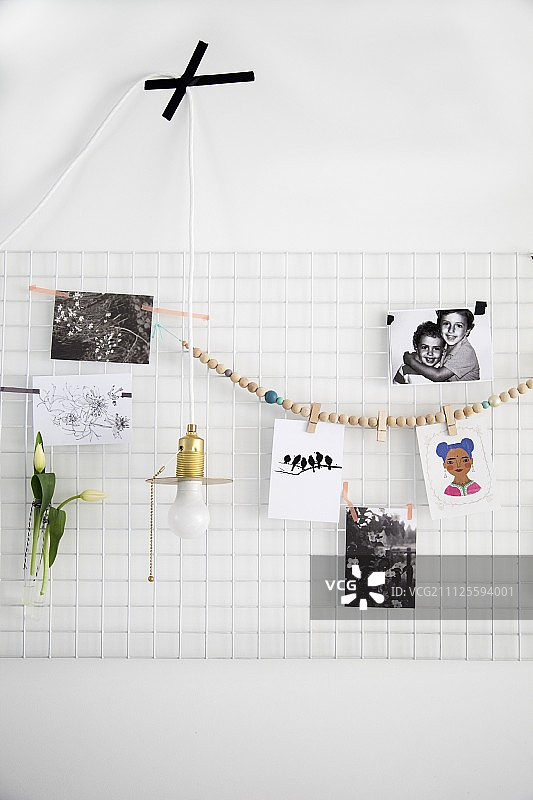 照片和珠子项链挂在白色金属网上，用作留言板，极简主义吊灯用黑色胶带粘在墙上图片素材