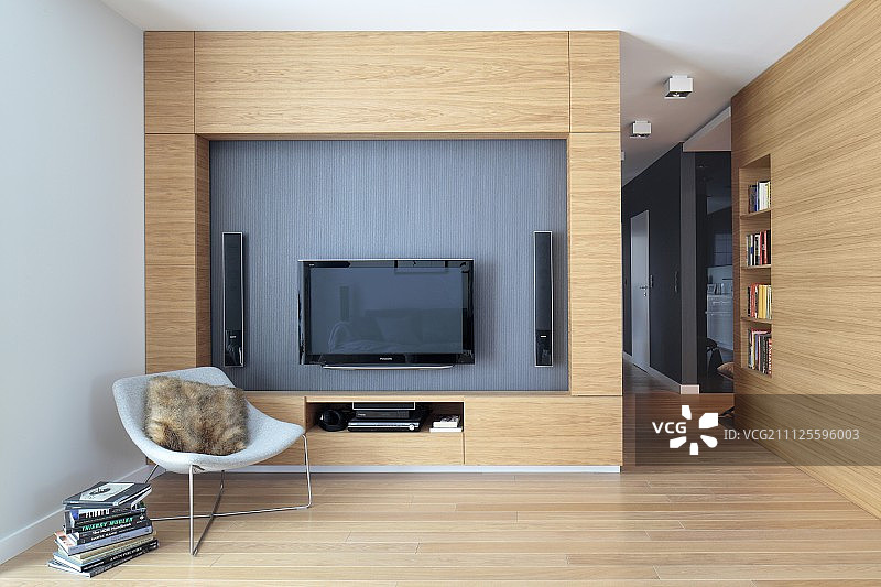 开放式室内，木制客厅墙壁前，带有平板电视和壁龛音箱的设计师扶手椅图片素材