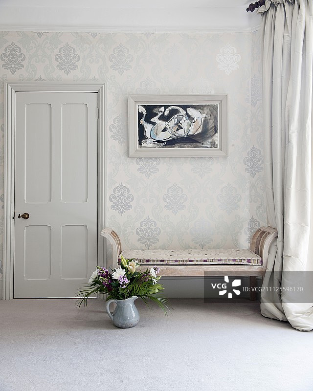 放在地板上靠着装饰墙的古董长凳旁的罐子里的花束图片素材