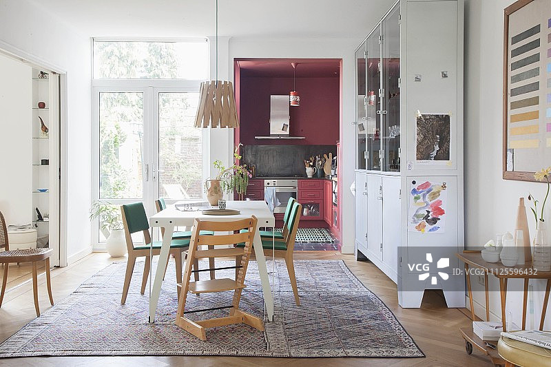 乡村风格的餐厅里，白色桌子周围环绕着Tripp Trapp高脚椅和复古椅子：背景是淡粉色的厨房图片素材