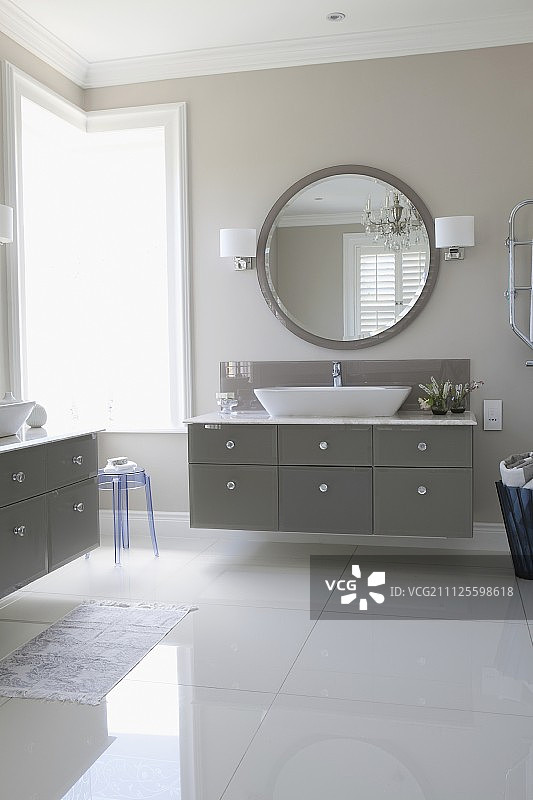 优雅的浴室，配有光亮的地板、灰色抽屉的盥洗台和大圆镜图片素材