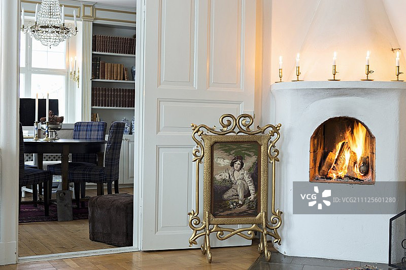 装饰华丽的镀金框挂毯防火屏，位于开放式壁炉和可通往餐厅的敞开门之间图片素材