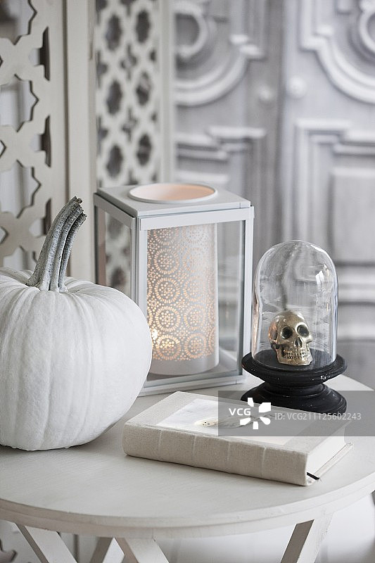 万圣节白色彩绘南瓜、玻璃罩下的骷髅装饰品和浪漫的烛台图片素材