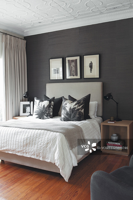 优雅卧室：双人床上排列着靠垫，高床头板搭配黑色壁纸图片素材