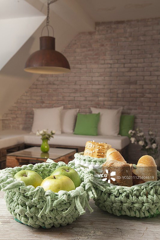 绿色钩针篮子里的水果和面包，位于砖墙前的木桌上图片素材