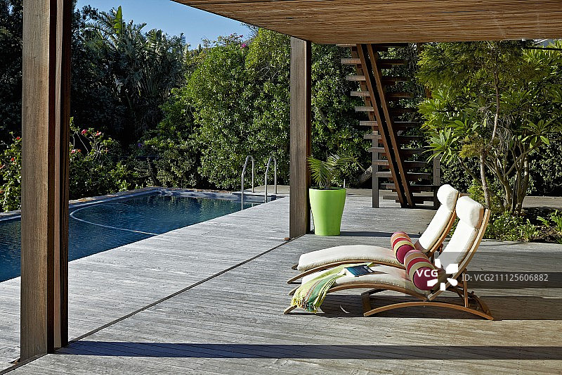 带淡色垫子和靠垫的日光浴躺椅，位于带屋顶的大型木制露台上图片素材