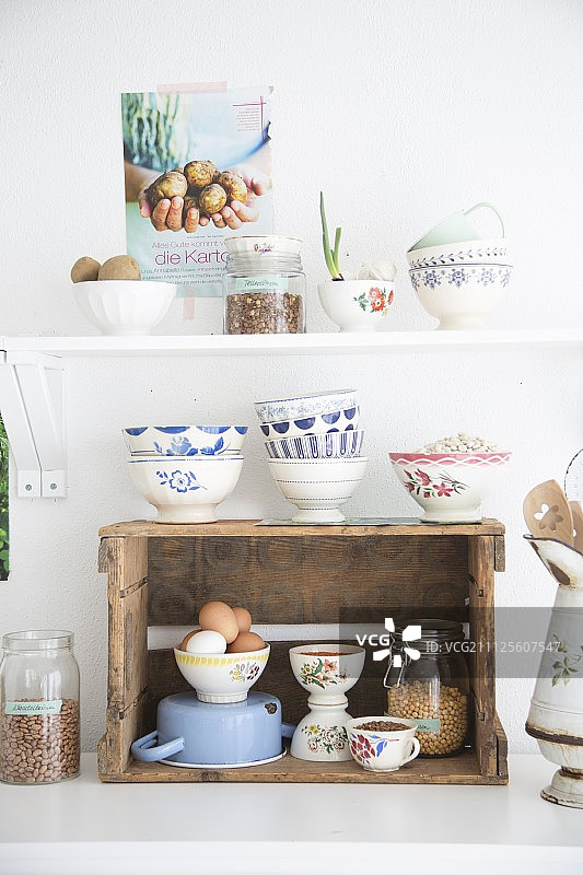 用作厨房搁板的复古葡萄酒箱和白色搁板下方堆叠的白色和蓝色碗，营造出复古风格的氛围图片素材