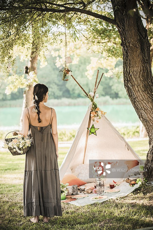 身穿夏季长裙的女人在浪漫野餐和圆锥形帐篷前手提花篮图片素材