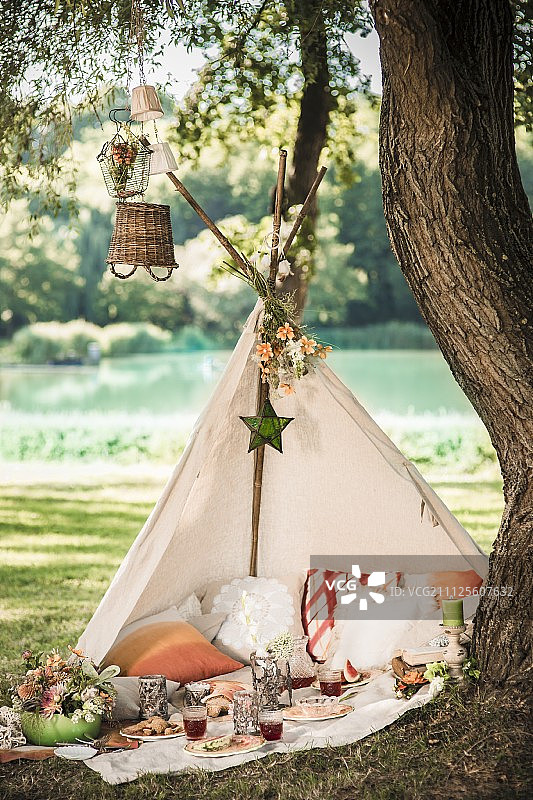 田园夏季风景中，树下开放式圆锥帐篷内的浪漫野餐图片素材