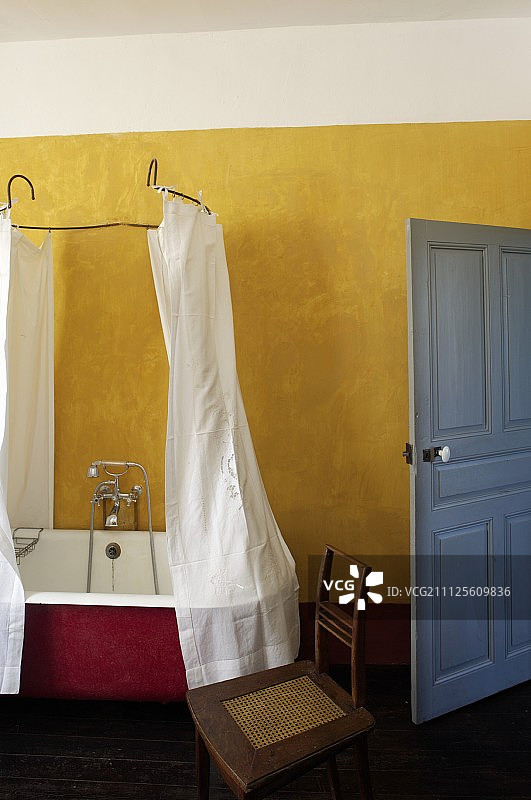 乡村浴室内的复古浴缸和金属框架浴帘，黄色墙壁和蓝色门图片素材