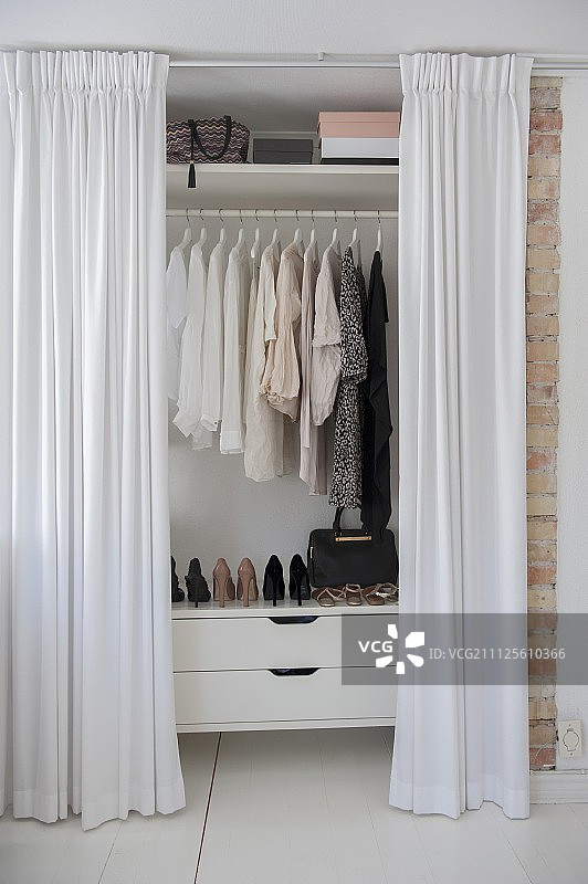 打开的及地白色窗帘遮住装满女装的衣柜图片素材