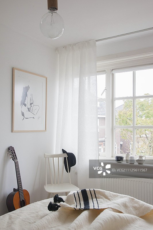 明亮卧室中格子窗旁的白色木椅和吉他图片素材