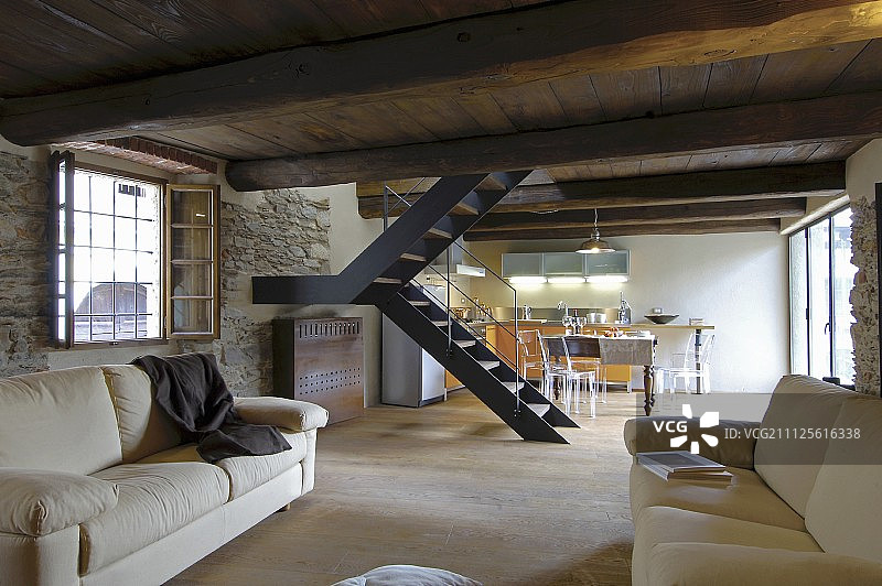 带横梁的木制天花板和乡村客厅的石墙，背景是楼梯和厨房餐厅图片素材