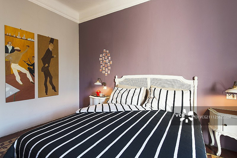 白色双人床搭配黑白条纹床单，背景为淡紫色墙壁图片素材