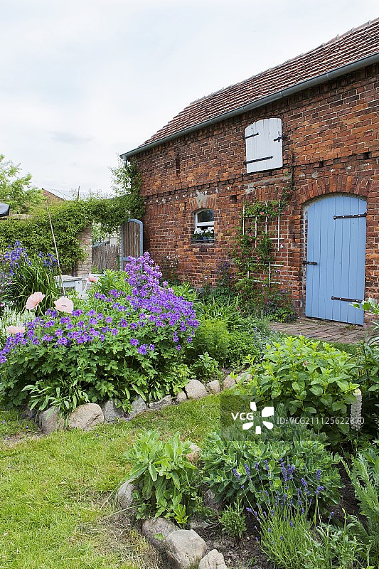 砖房，四周环绕着带石砌花坛的乡村花园图片素材
