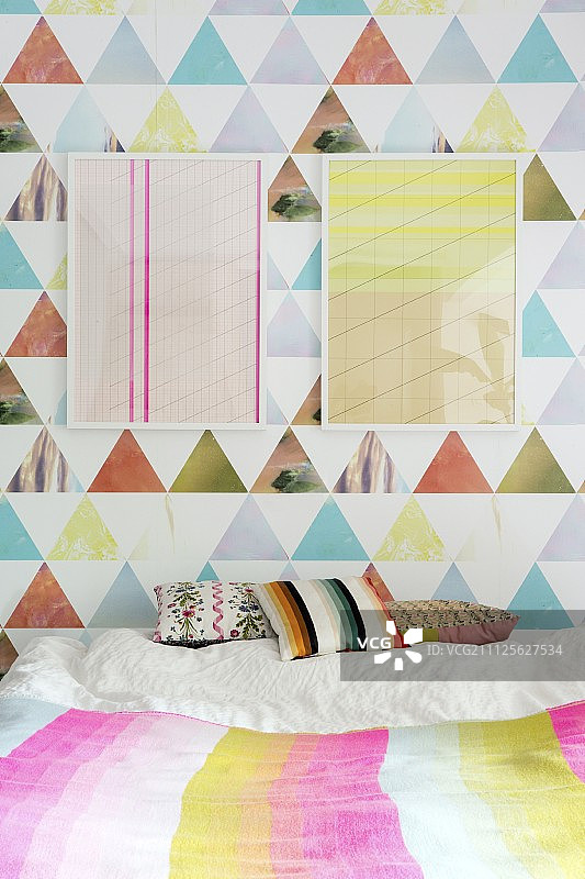 床上靠垫上方彩色壁纸上的两幅框架图形艺术品图片素材