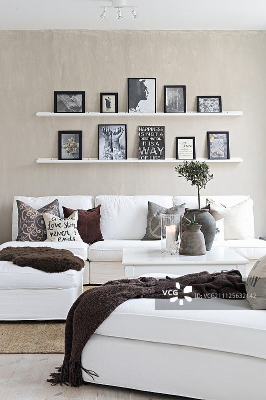 米色墙壁上，窄架子上摆放着白色沙发和泥土色调的装饰品图片素材