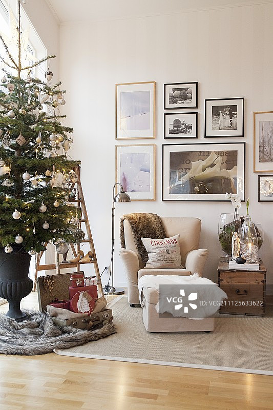 客厅里米色扶手椅、脚凳和墙上挂满相框的装饰圣诞树图片素材