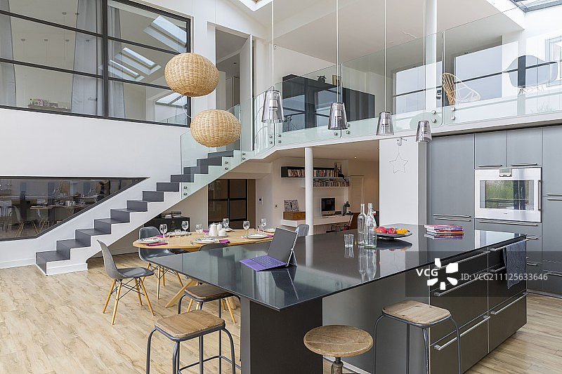 阁楼公寓开放式厨房中的黑色台面和带玻璃栏杆的走廊图片素材